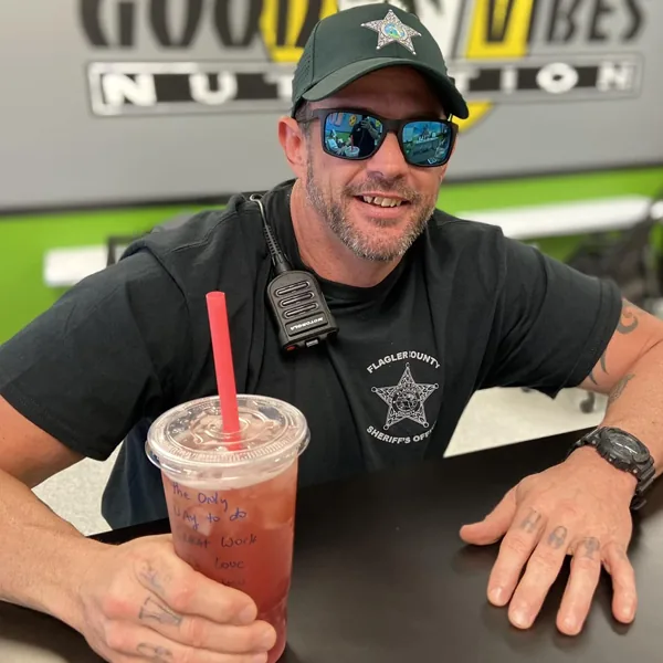 A smiling Flagler County Sheriff's Office deputy holds a large iced drink with a red straw.