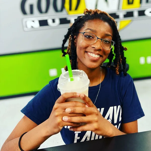 A customer with glasses and braids smiles while holding a shake with a green straw.