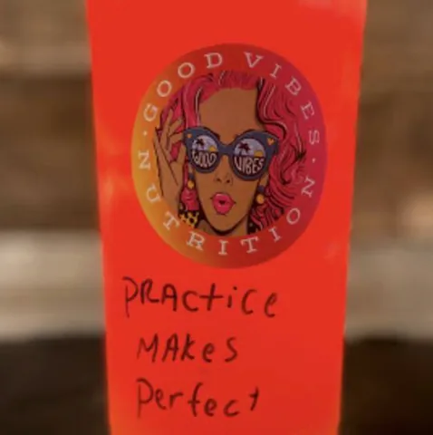 A bright red Jolly Sunset power tea with 'Practice makes perfect' written on the cup.